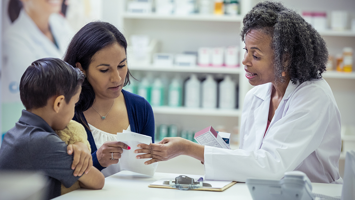 Mature pharmacist hands a mid adult woman a prescription medication. The pharmacist reviews instructions for taking the medication.