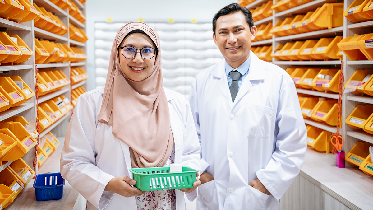 Portrait of Malaysian female and male health specialists standing in hospital pharmacy, looking at camera holding a supply of medication