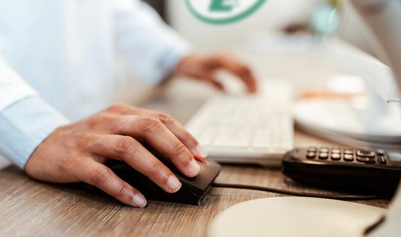 Closeup of pharmacist's hands typing on a computer keyboard at the pharmacy counter.
