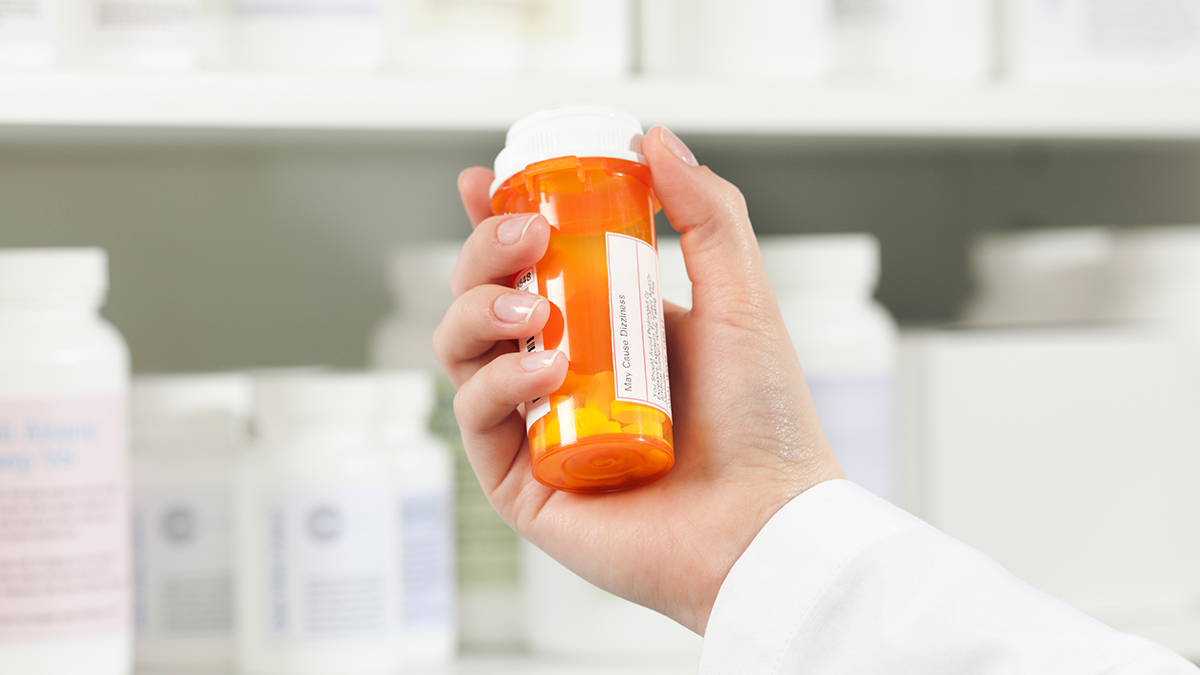 pharmacist's hand holding a prescription medication bottle