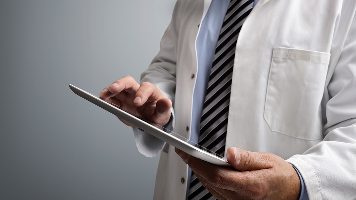 Doctor using digital tablet on gray background